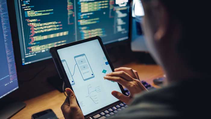 White man programmer or IT specialist software developer with glasses working late into the night examining UX UI flowcharts and design wireframes for a mobile app,integrating design and development on dual monitors computer